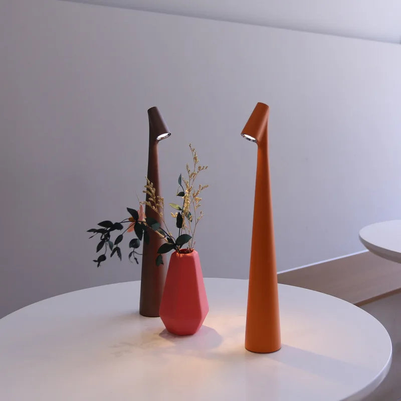 Glow Tube Cordless Lamps in brown and orange glowing on a white table beside a pink vase