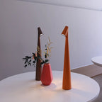 Glow Tube Cordless Lamps in brown and orange glowing on a white table beside a pink vase