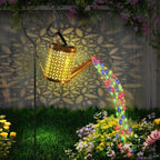 Solar Watering Can Garden Lantern glowing over garden flowers