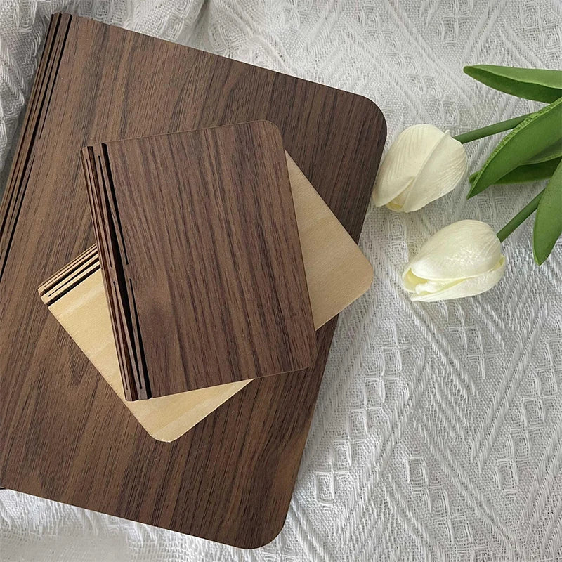 Storybook Folding Book Lamp closed, showing its wooden cover, beside white flowers